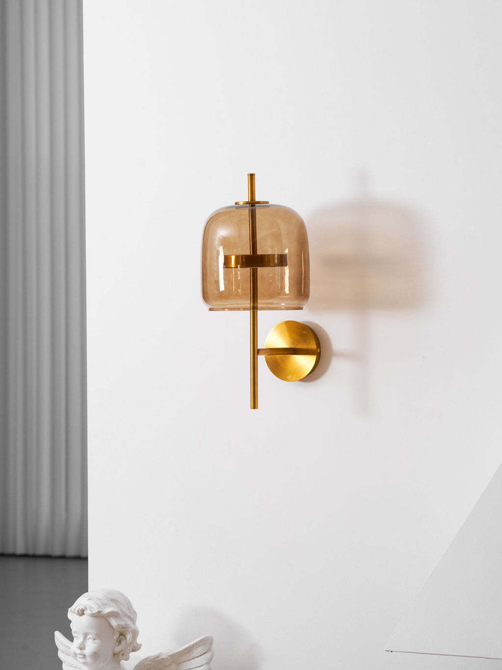 Gold & Coffee Clérachic wall light on a white wall, with a pale curtain at the left and a cherub statue at the bottom edge.