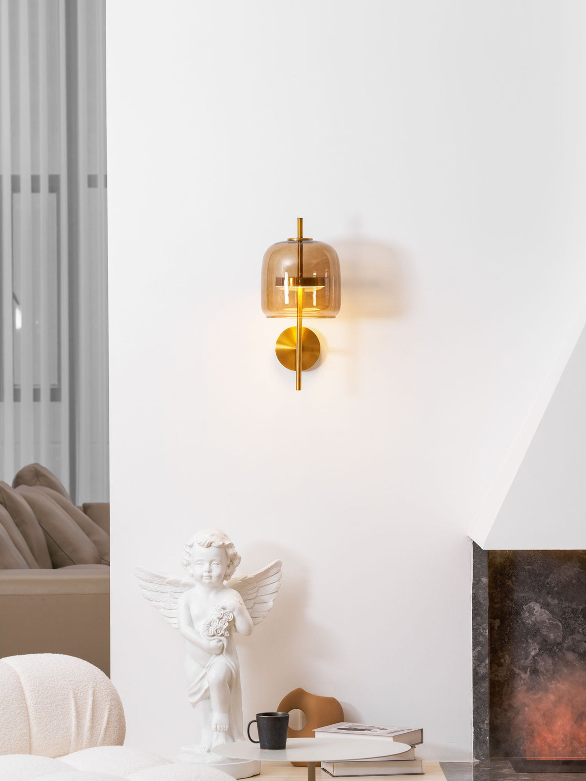This Clérachic wall light glows on a white wall, with a cherub statue, a black mug and a stone fireplace below it.