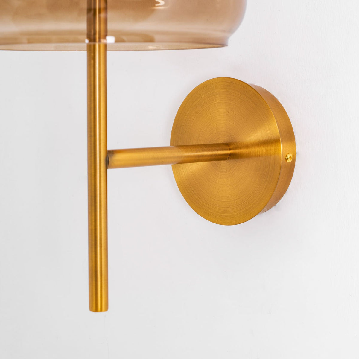 Close view of the brushed gold round backplate and the arm joining the stem on this Clérachic wall light.