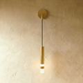 Clérachic brushed brass-toned wall light with a round backplate, slim cord and a cylinder with a frosted glow, on limewash.
