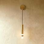 Clérachic brushed brass-toned wall light with a round backplate, slim cord and a cylinder with a frosted glow, on limewash.