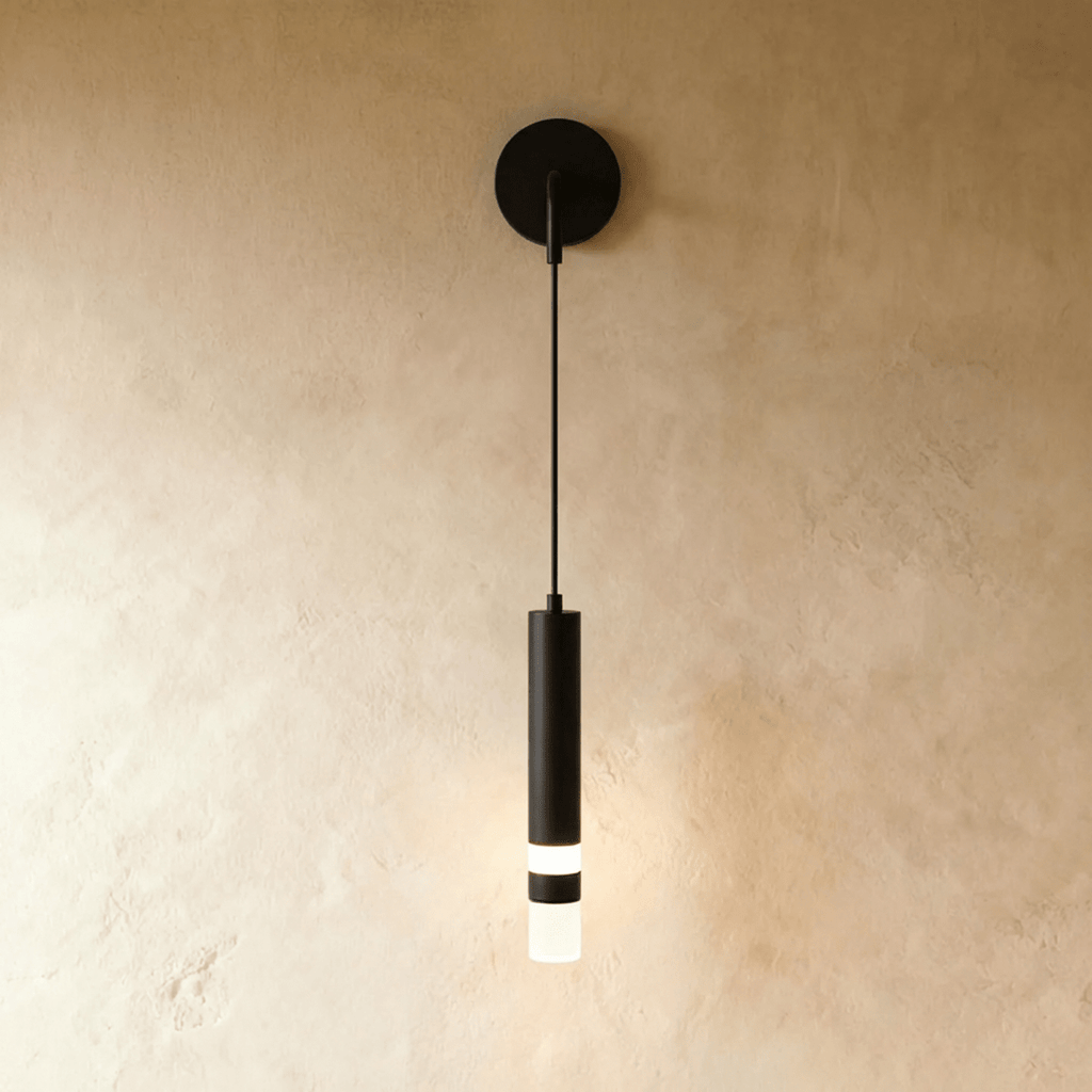 Clérachic matte black wall light with a round backplate, thin cord and a slim cylinder with a lit frosted band, on limewash.