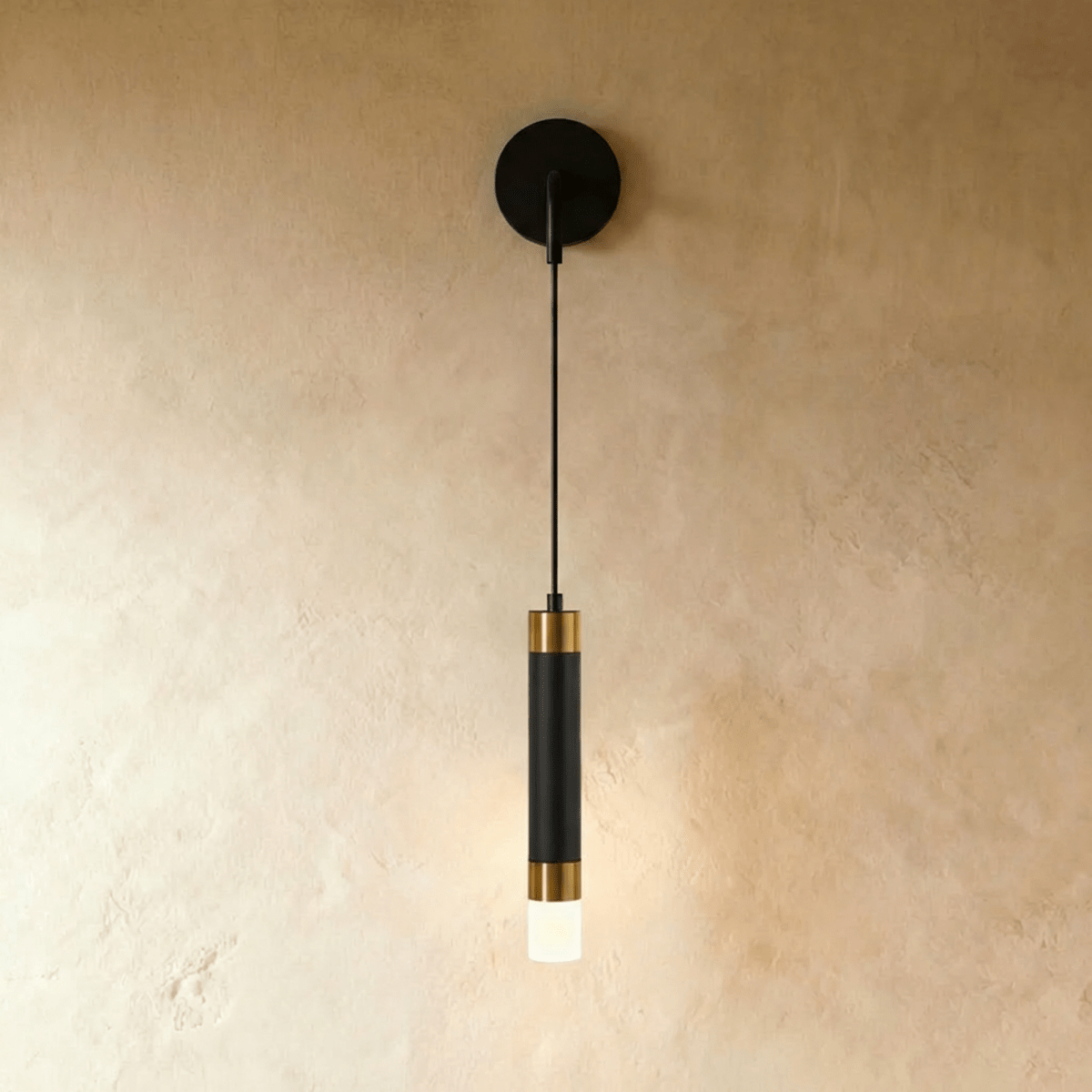 Clérachic wall light with a black backplate and cord, a black cylinder capped in brass-toned bands and a frosted tip.