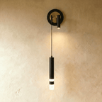 Clérachic wall light with a black ring backplate framing a brass-toned disc, a spotlight head and a black hanging cylinder.