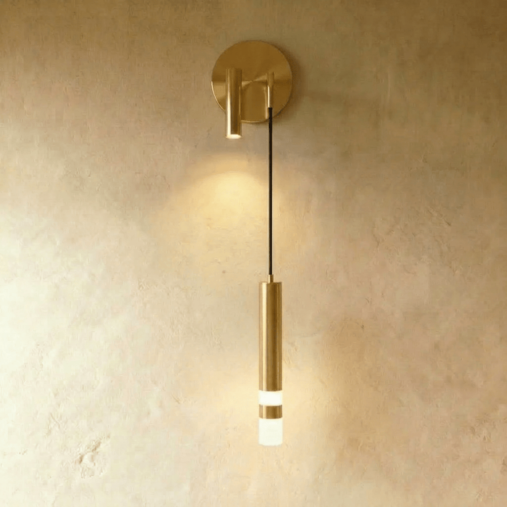 Clérachic brass-toned wall light with a round backplate, a spotlight on the opposite side and a lit hanging cylinder.