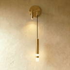 Clérachic brass-toned wall light with a round backplate, a spotlight on the opposite side and a lit hanging cylinder.