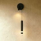 Clérachic matte black wall light with a round backplate, a spotlight on the left and a hanging cylinder with a glowing band.