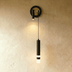 Clérachic wall light with a black ring backplate around a brass-toned disc, a black spotlight and a black hanging cylinder.