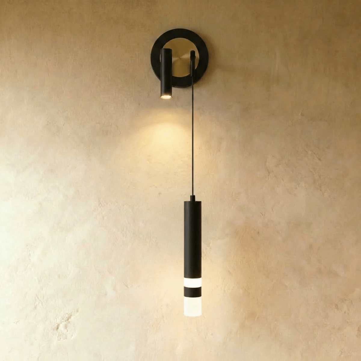 Clérachic wall light with a black ring backplate around a brass-toned disc, a black spotlight and a black hanging cylinder.