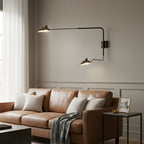 Clérachic two-arm black wall light above a tan leather sofa with cream cushions, on a taupe panelled wall.