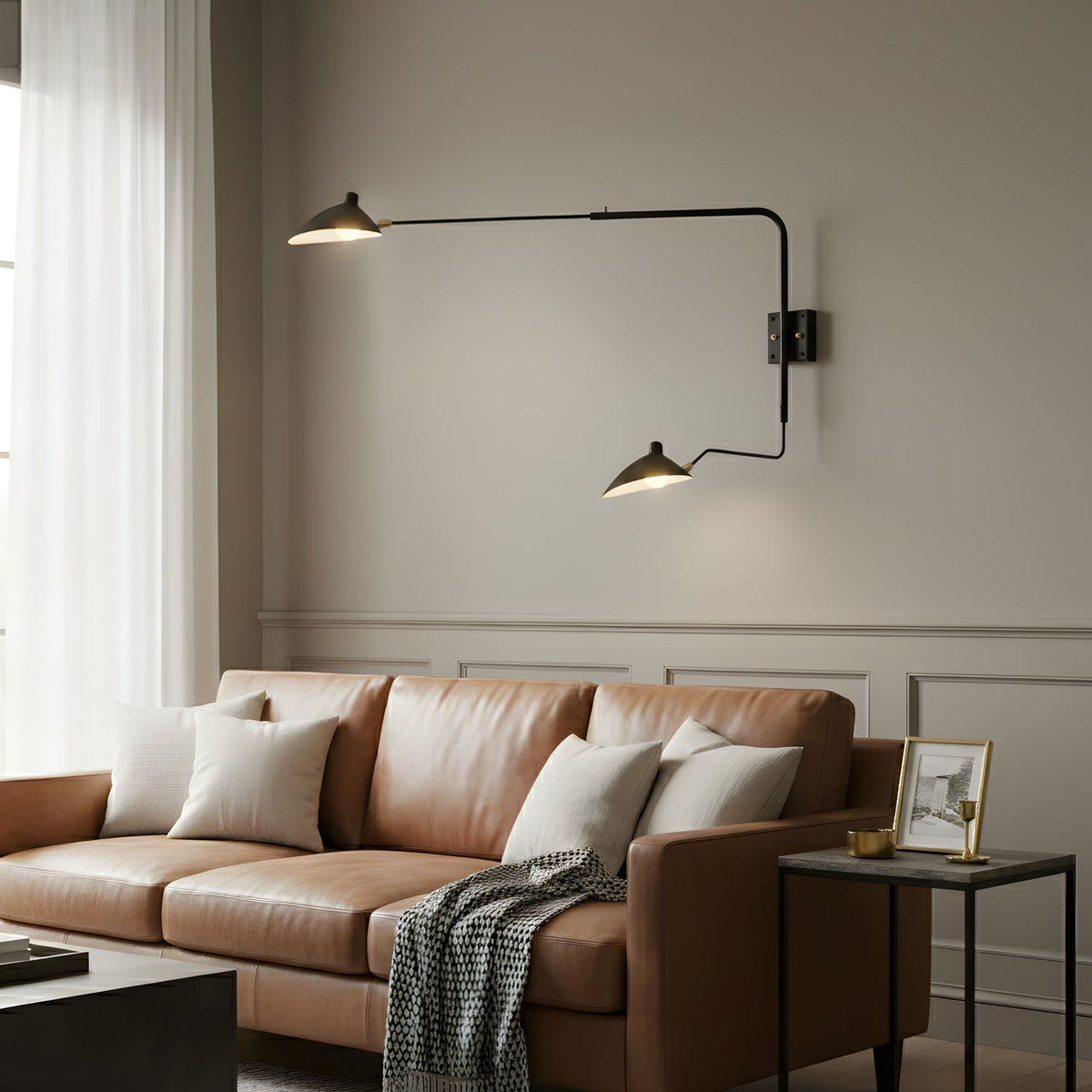 Clérachic two-arm black wall light above a tan leather sofa with cream cushions, on a taupe panelled wall.