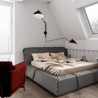 A Clérachic black wall light above a houndstooth bed in an attic bedroom, with one head angled upward and one out to the side.