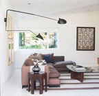 Clérachic two-head wall light with very long arms spanning a white wall, above a plum corner sofa and a glass coffee table.