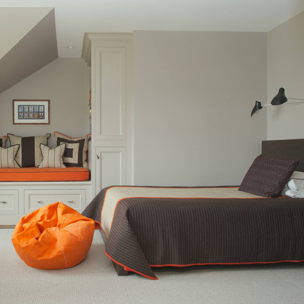 Clérachic black wall light above a bed in an attic room, with a patterned bedspread and a bright orange bean bag beside it.