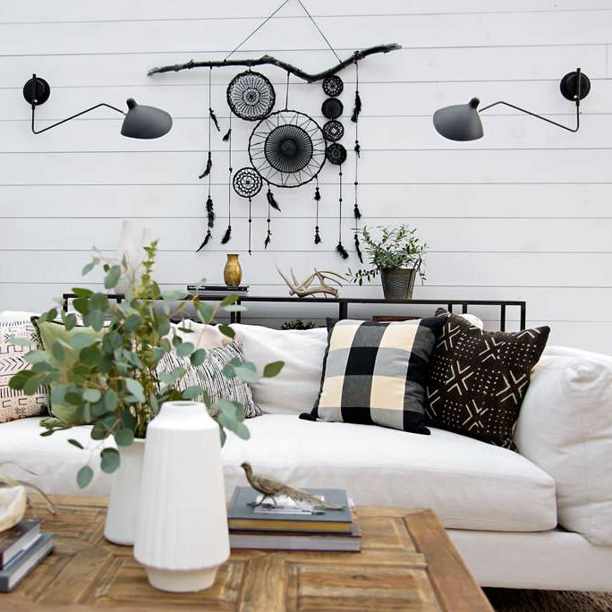 Pair of Clérachic wall lights with long black arms on a white shiplap wall, above a white sofa and a rustic wood coffee table.