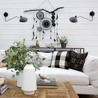 Pair of Clérachic wall lights with long black arms on a white shiplap wall, above a white sofa and a rustic wood coffee table.