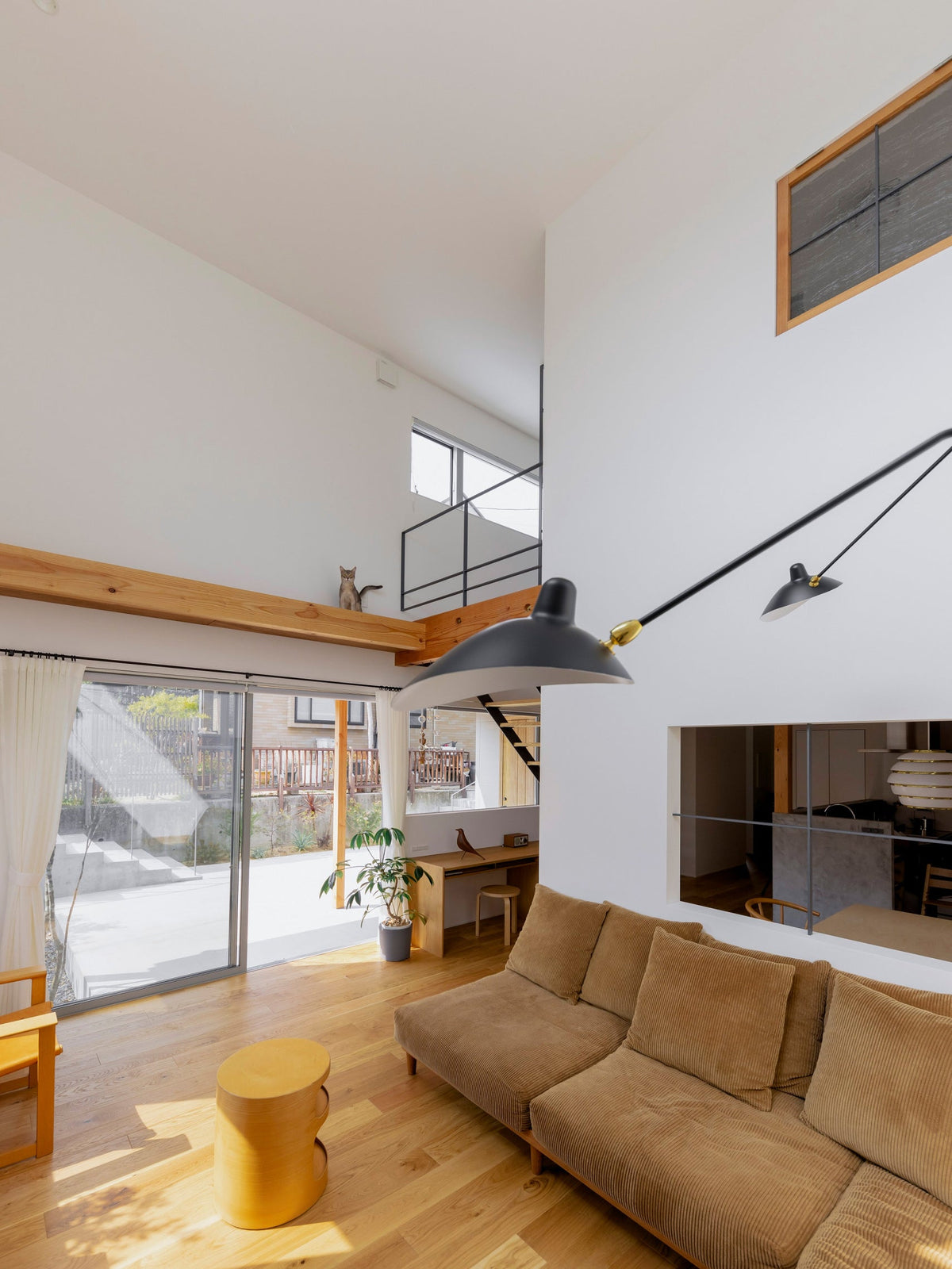 Large Clérachic black wall light with a cone shade, projecting from a tall white wall above tan sofas and a glass sliding door.
