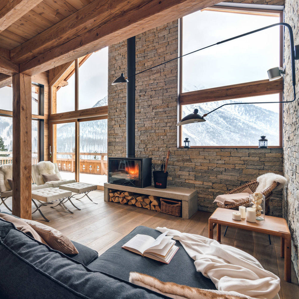 Clérachic black wall light with extra-long arms in a chalet living room with stone walls, timber beams and a wood-burning stove.