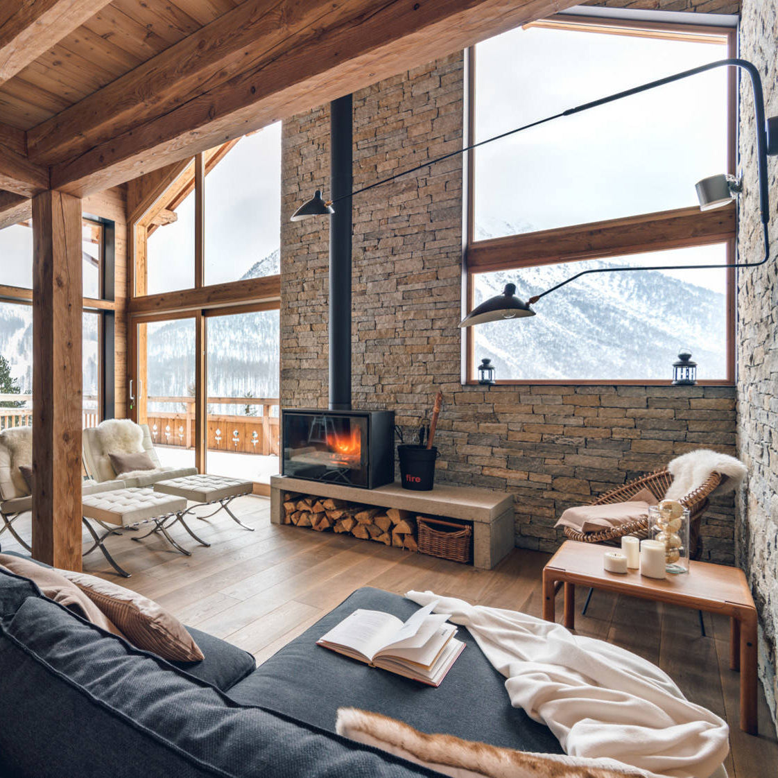 Clérachic black wall light with extra-long arms in a chalet living room with stone walls, timber beams and a wood-burning stove.