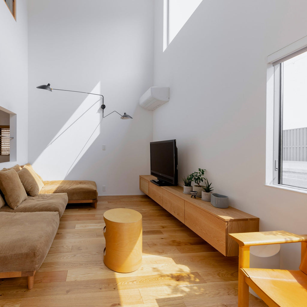 Clérachic wall light with two long arms in a tall white room, above a low tan sofa and a wooden TV unit.
