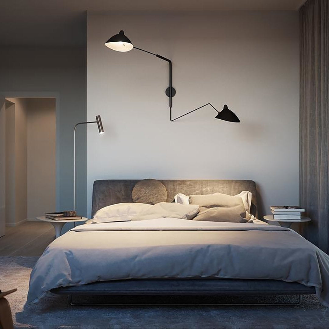 Large Clérachic black wall light above a grey upholstered bed in a dim bedroom, with a reading lamp at the side.