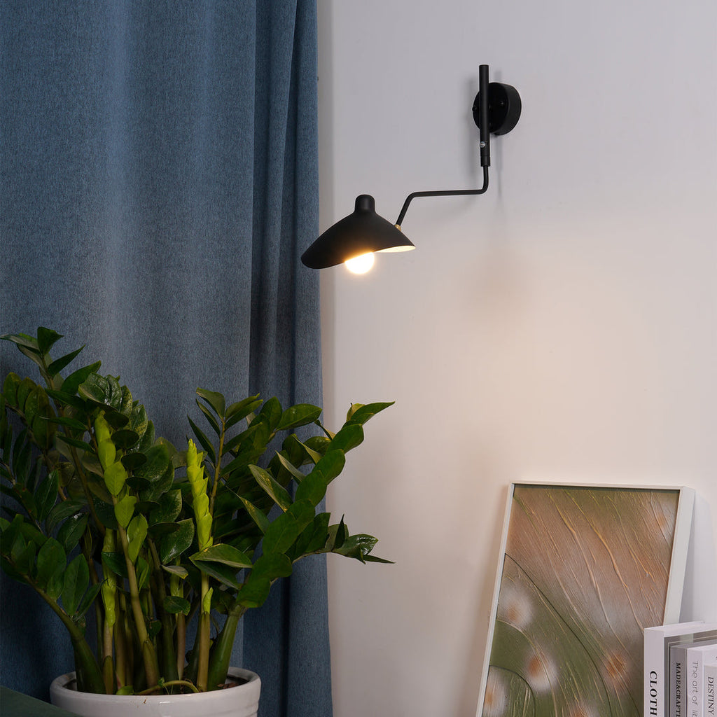 Clérachic black wall light with a cone shade and a curved arm, on a pale wall beside a blue curtain and a green plant.