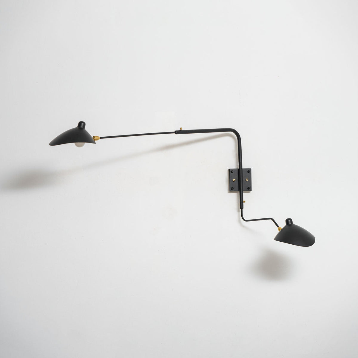 Clérachic two-head wall light on a white wall, unlit, with a soft shadow beneath the cone shades.