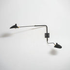 Clérachic two-head wall light tilted to the side on a white wall, with a dark shadow behind the long arm.