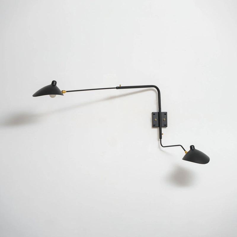 Clérachic two-head wall light tilted to the side on a white wall, with a dark shadow behind the long arm.