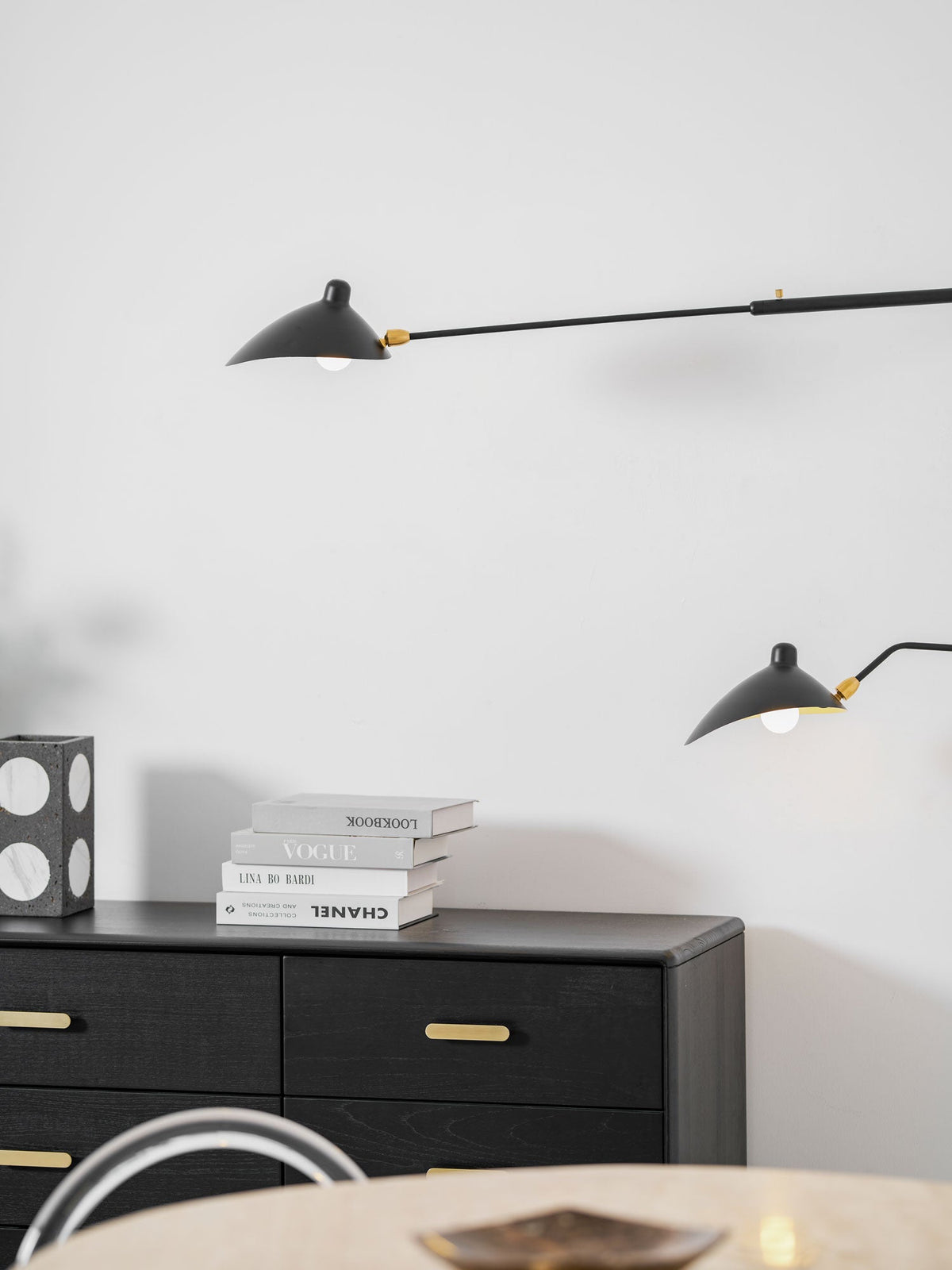 Close view of the cone head and brass joint on this Clérachic wall light, with books on a black chest below.