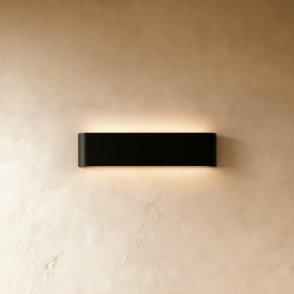 Clérachic slim black aluminium wall light on a warm limewash wall, glowing softly above and below its rounded ends.