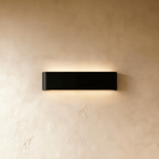 Clérachic slim black aluminium wall light on a warm limewash wall, glowing softly above and below its rounded ends.