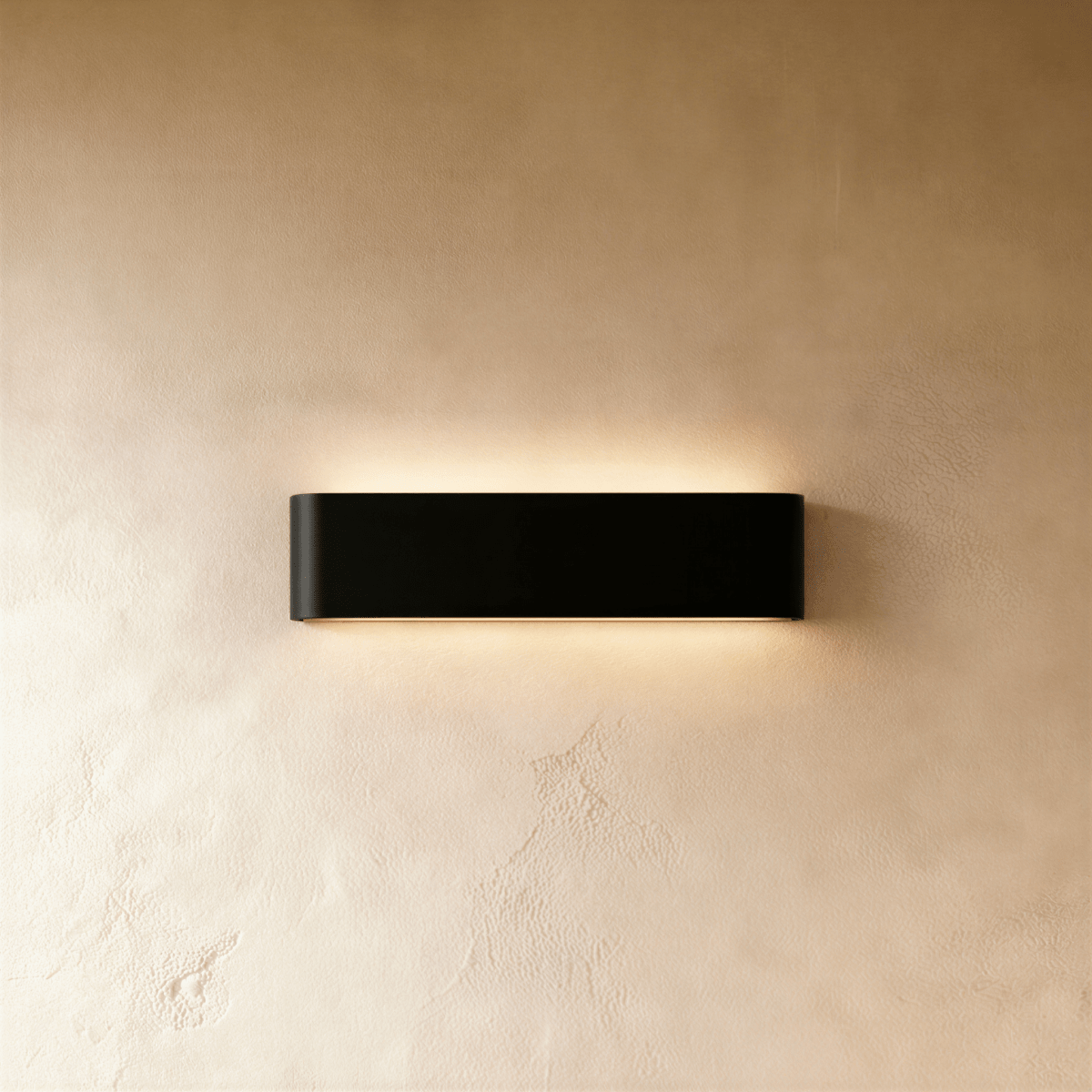 Clérachic slim black aluminium wall light on a warm limewash wall, glowing softly above and below its rounded ends.