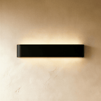 Clérachic longer black aluminium wall light with rounded ends, throwing soft light above and below onto cream plaster.