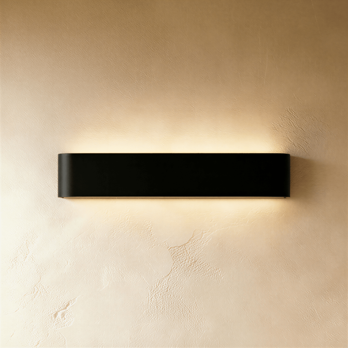 Clérachic longer black aluminium wall light with rounded ends, throwing soft light above and below onto cream plaster.