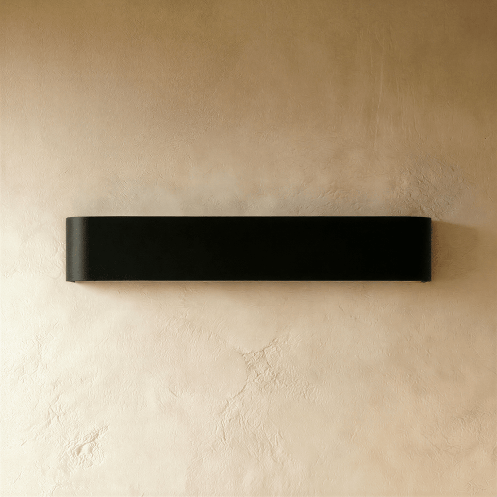 Clérachic long black aluminium wall light switched off on a warm plaster wall, showing its matte finish and rounded edges.