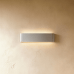 Clérachic slim brushed silver aluminium wall light with rounded ends, lit above and below against warm plaster.
