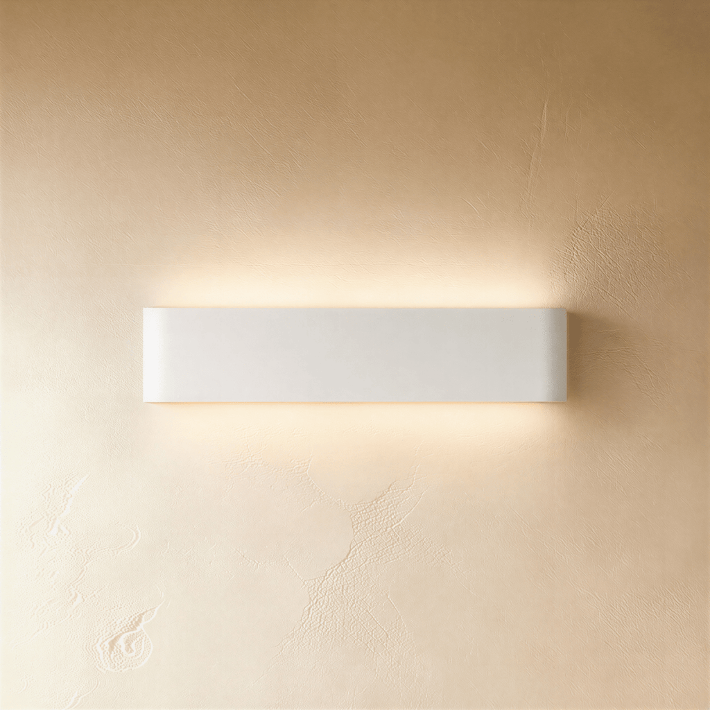 Clérachic white aluminium wall light in a medium length, lit up and down against a softly textured limewash wall.