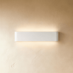 Clérachic white aluminium wall light in a medium length, lit up and down against a softly textured limewash wall.