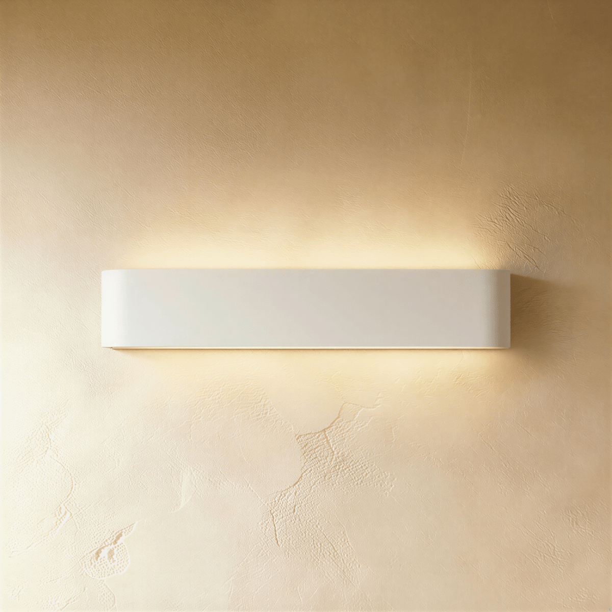 Clérachic longer white aluminium wall light with rounded ends, glowing warmly above and below on a plaster wall.