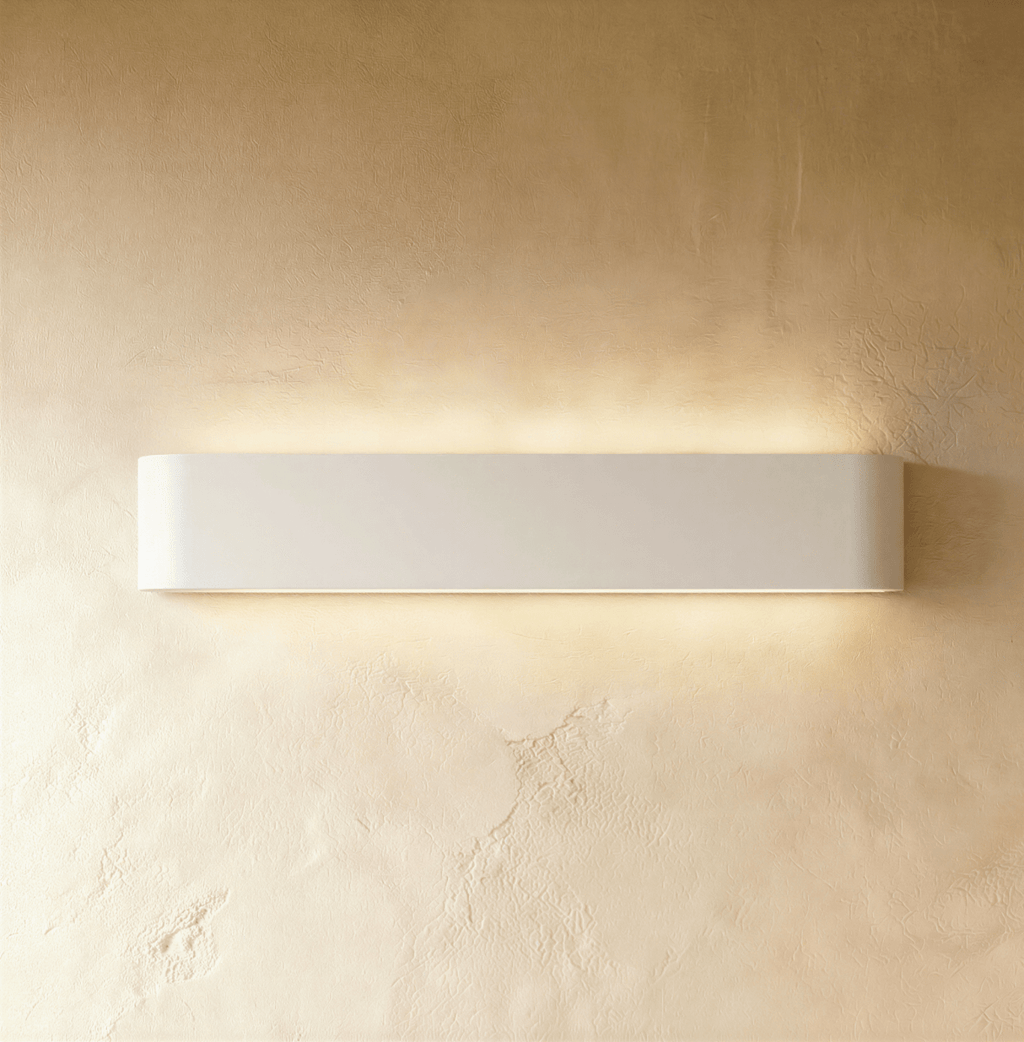Clérachic long white aluminium wall light lit, a wide band of warm light spreading over golden textured plaster.