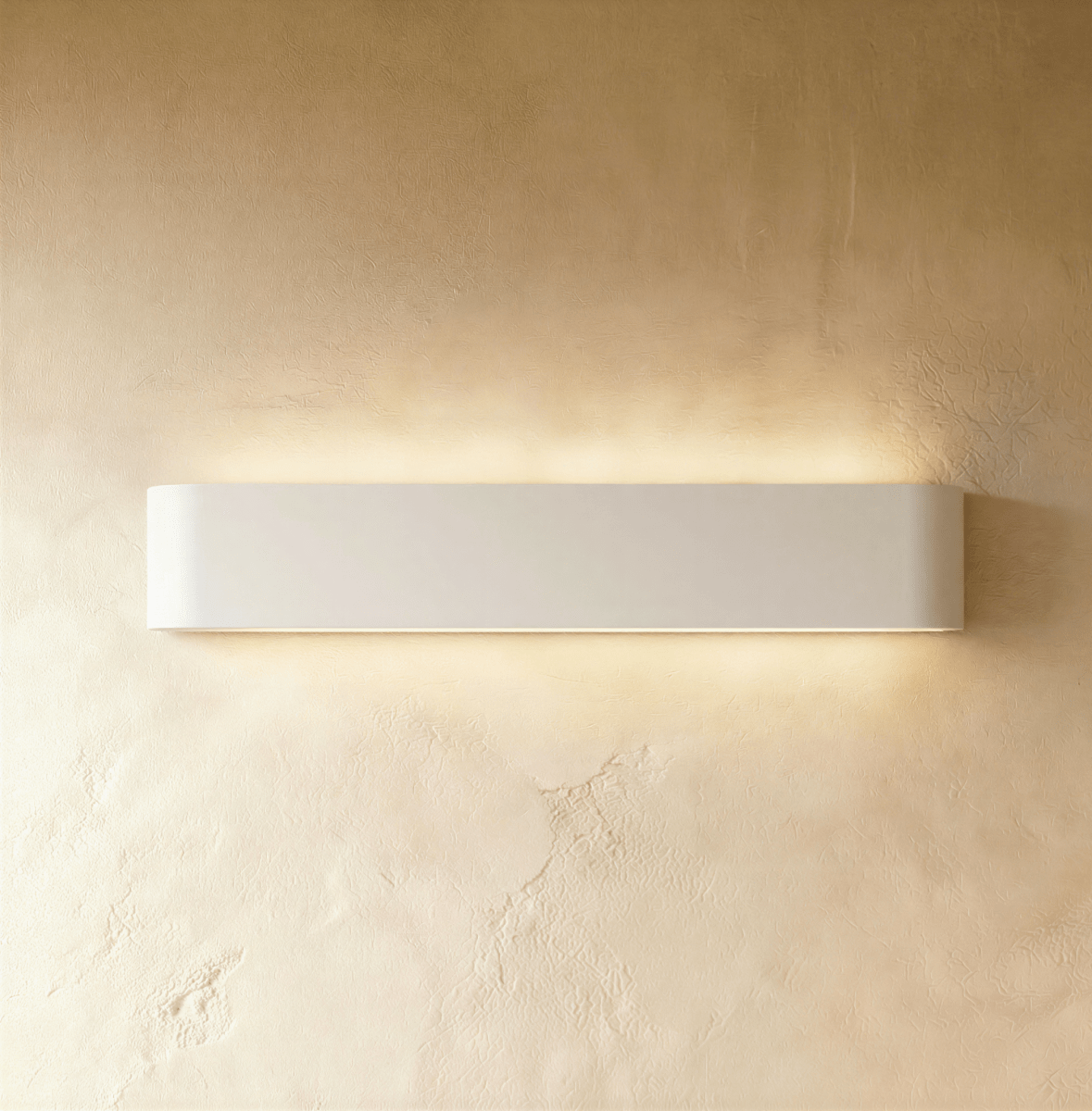 Clérachic long white aluminium wall light lit, a wide band of warm light spreading over golden textured plaster.