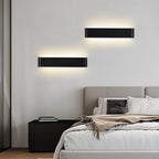 Clérachic pair of black aluminium wall lights staggered above a bedside table and upholstered bed in a calm grey bedroom.