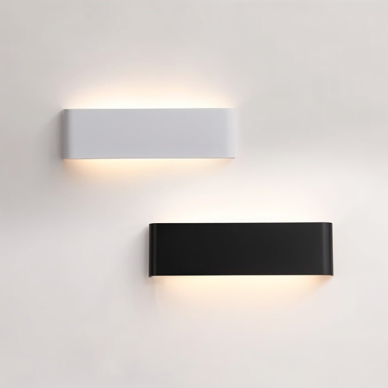 Clérachic white and black aluminium wall lights side by side on a pale wall, each glowing softly above and below.