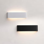 Clérachic white and black aluminium wall lights side by side on a pale wall, each glowing softly above and below.