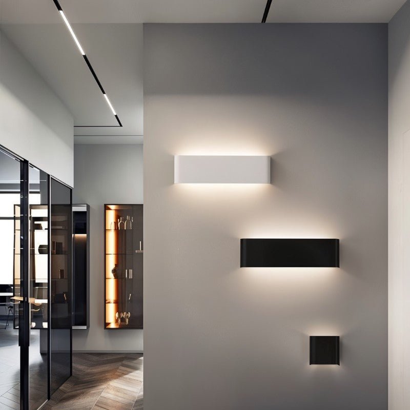 Clérachic white and black aluminium wall lights in three lengths on a grey hallway wall beside a glass display cabinet.