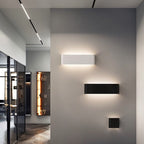 Clérachic white and black aluminium wall lights in three lengths on a grey hallway wall beside a glass display cabinet.