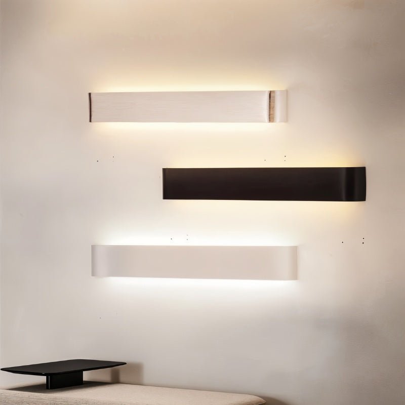 Clérachic brushed silver, black and white aluminium wall lights stacked on a cream wall above a low bench.