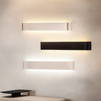 Clérachic brushed silver, black and white aluminium wall lights stacked on a cream wall above a low bench.
