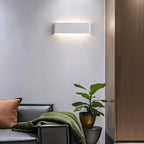 Clérachic white aluminium wall light on a pale wall above a leather sofa, a green throw and a potted plant.